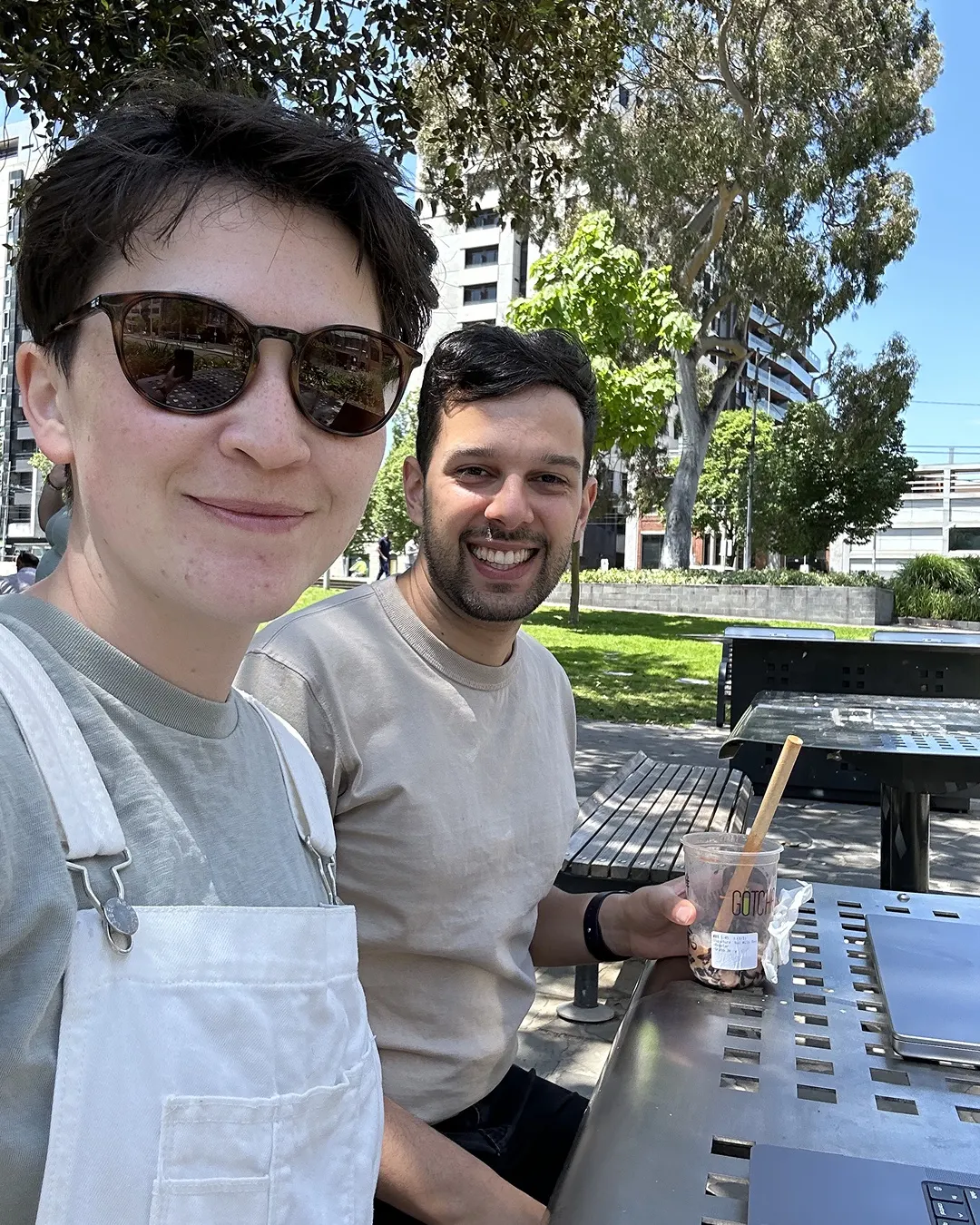 Brie and Sherv working at an outdoor table, with a laptop and a bubble tea